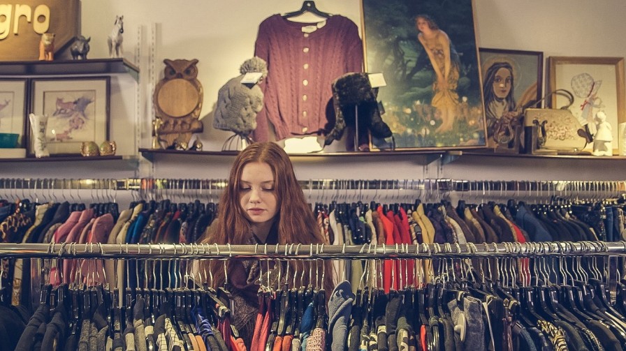 A woman examines various clothing items while browsing in a clothing store, showcasing her interest in fashion choices.